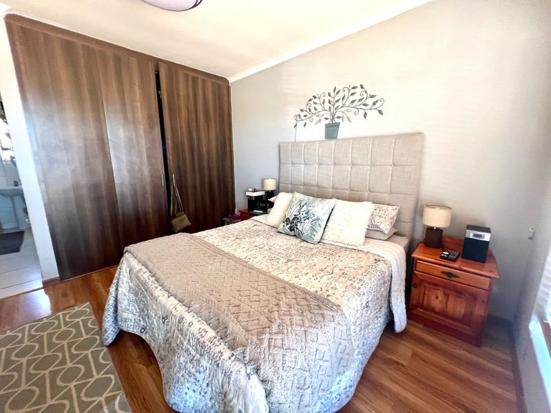A bedroom featuring laminate flooring and built-in wooden cupboards, with an adjacent view into a tiled bathroom area.