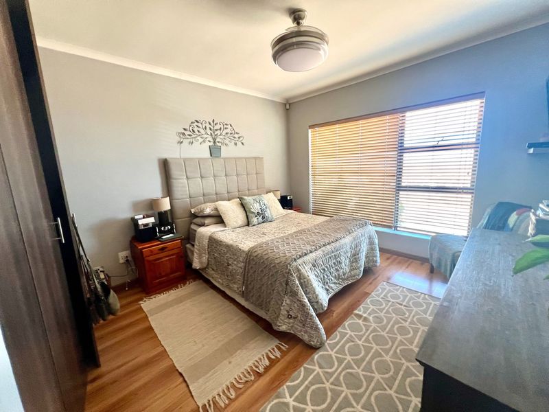 A well-maintained bedroom featuring laminate flooring, a ceiling fan, and large windows with fitted venetian blinds.