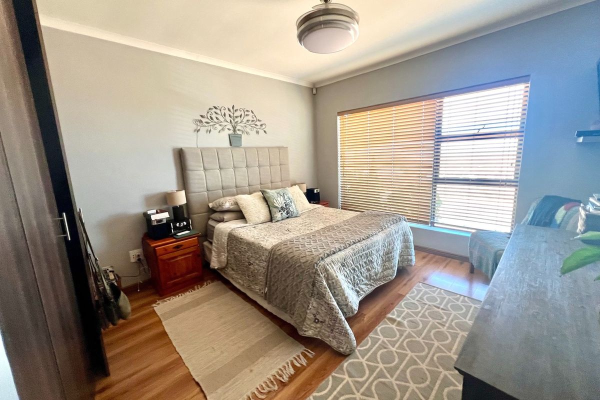 A well-maintained bedroom featuring laminate flooring, a ceiling fan, and large windows with fitted venetian blinds.