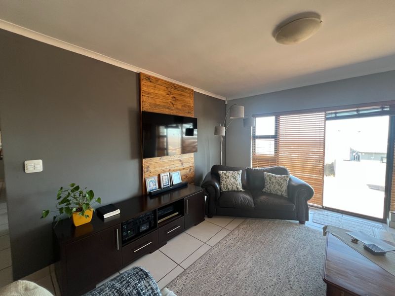 A comfortable living room featuring tiled floors, a timber accent wall for the television, and large sliding glass doors providing natural light.