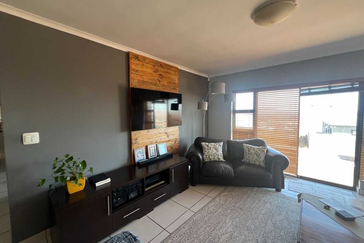 A comfortable living room featuring tiled floors, a timber accent wall for the television, and large sliding glass doors providing natural light.