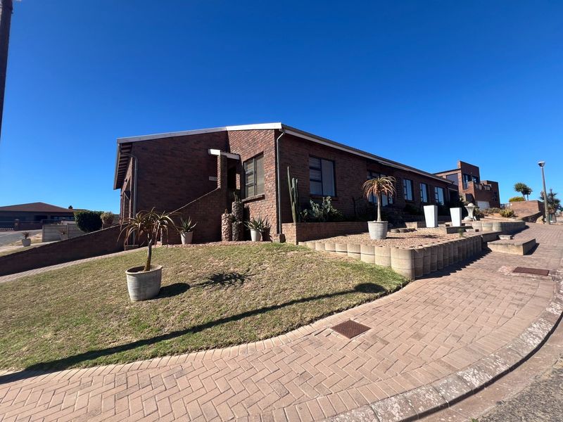 A well-maintained face brick house featuring a paved driveway, tiered retaining walls, and a landscaped front garden under a clear blue sky.