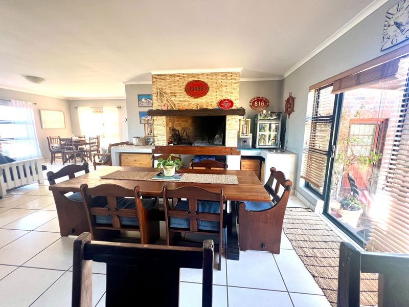 Spacious open-plan living and dining area featuring a prominent stone-clad indoor braai, tiled flooring, and large sliding doors providing natural light.