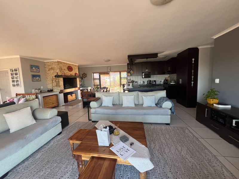 Spacious open-plan living area featuring a built-in stone fireplace, tiled flooring, and a modern kitchen with dark cabinetry and a central island.