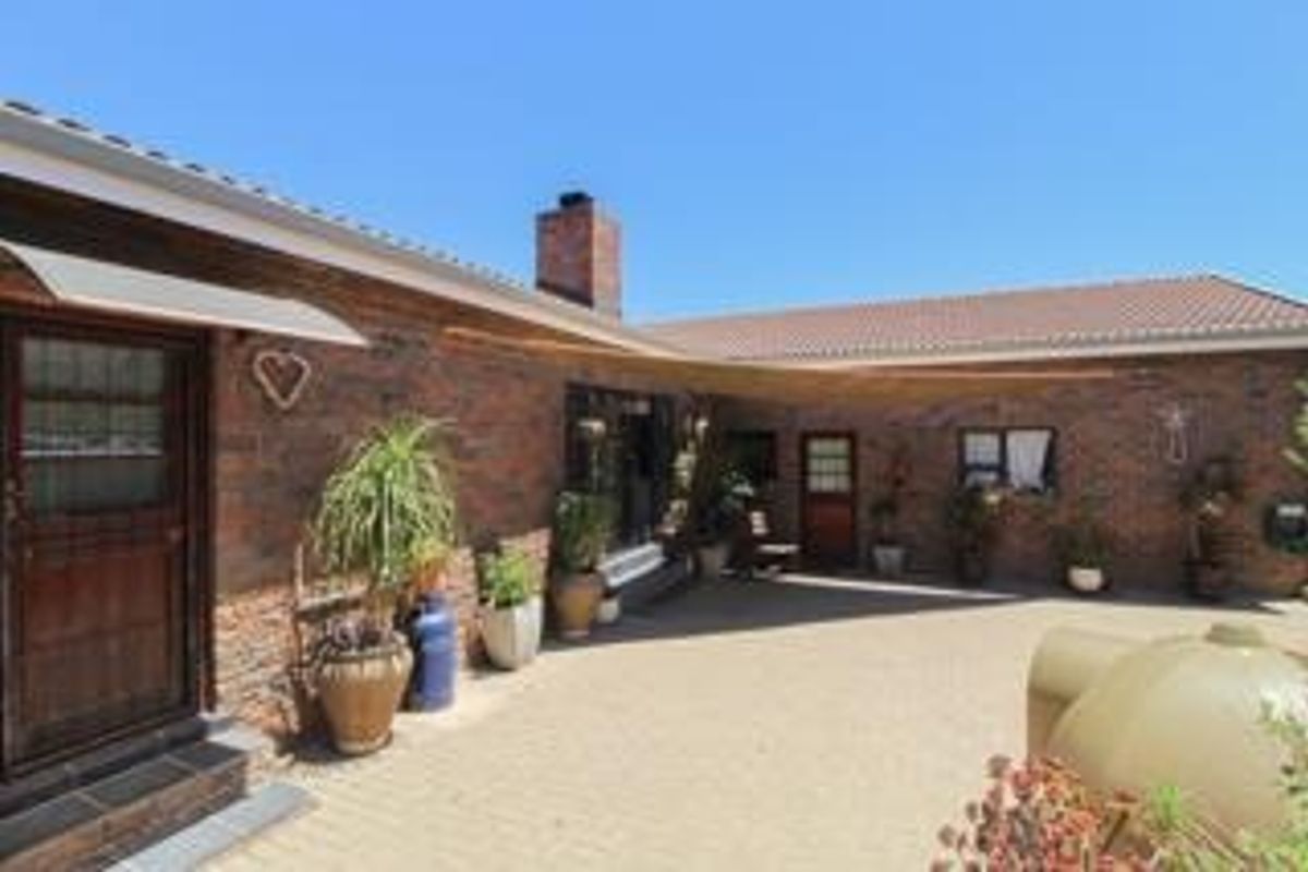 A rear exterior view of a brick house featuring a paved courtyard area, tiled roofing, and a chimney.