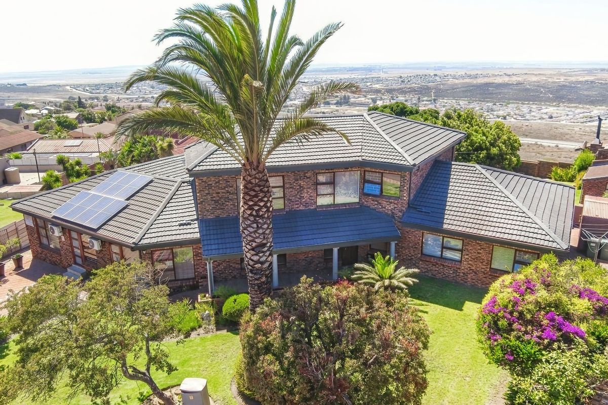 Aerial view of a double-story brick house featuring a tiled roof, integrated solar panels, and a well-maintained garden with mature palm trees.