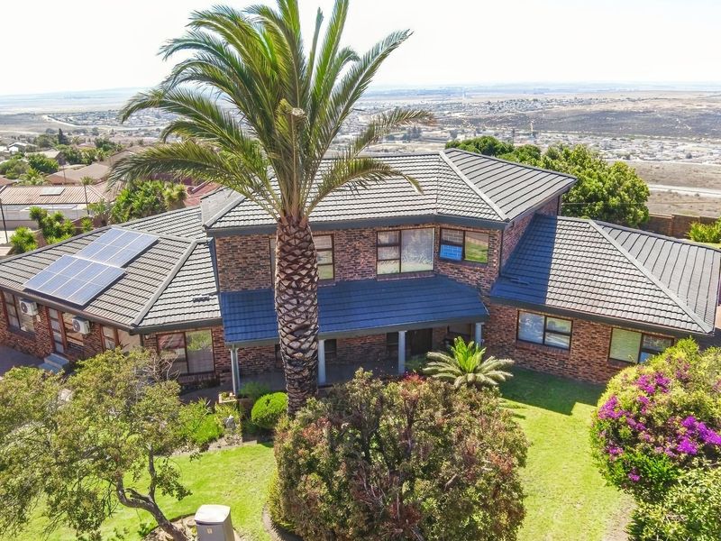 Aerial view of a double-story brick house featuring a tiled roof, integrated solar panels, and a well-maintained garden with mature palm trees.