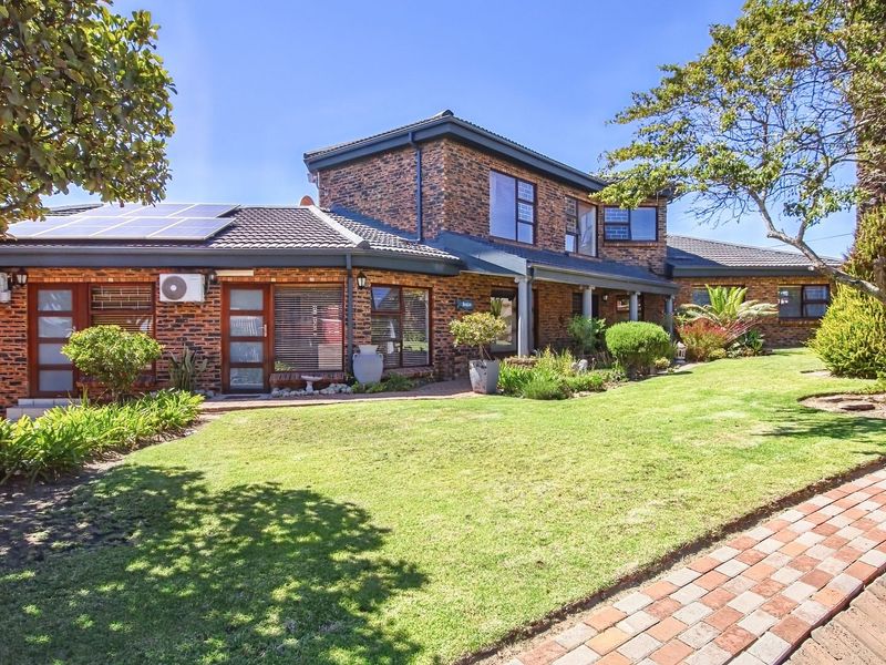 A well-maintained face brick house featuring a landscaped front garden, paved walkway, and roof-mounted solar panels under a clear blue sky.
