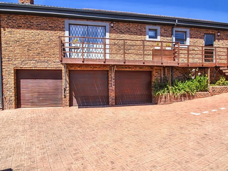 Front exterior view featuring a face brick facade, three garage doors, and a raised wooden deck with staircase access.
