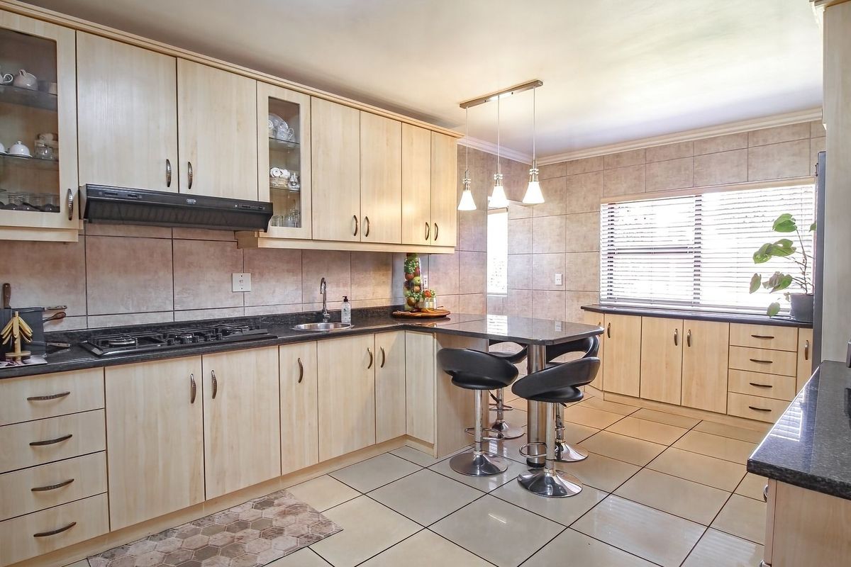 A functional kitchen featuring light wood cabinetry, granite countertops, a gas hob with extractor, and a convenient breakfast nook with tiled flooring throughout.