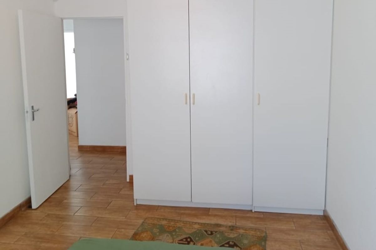 A bedroom featuring neutral white walls, tiled flooring, and a large built-in wardrobe with clean lines.
