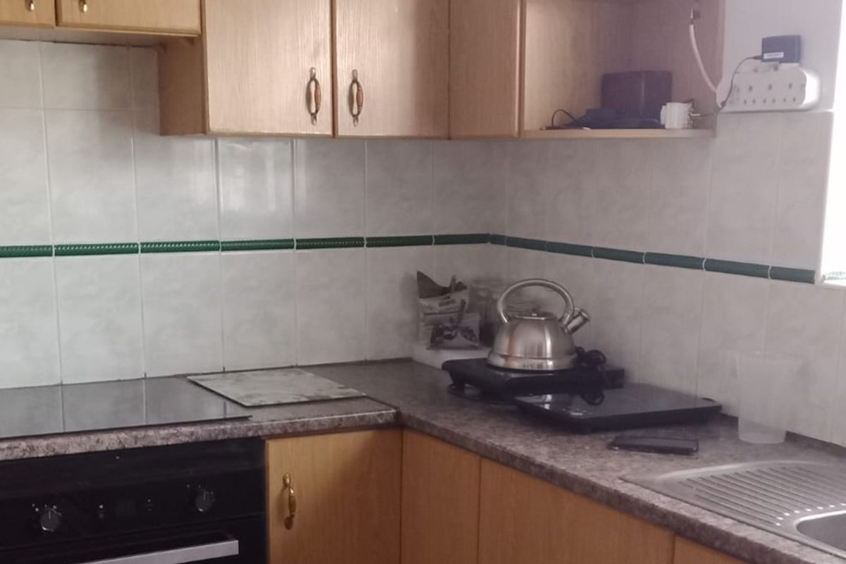 A functional kitchen featuring laminate cabinetry, tiled splashbacks, a built-in oven with electric hob, and a stainless steel sink.