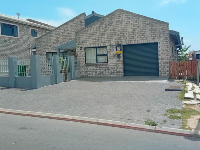 Front exterior view of a face brick house featuring a paved driveway, secure boundary wall, and a roller shutter garage door.