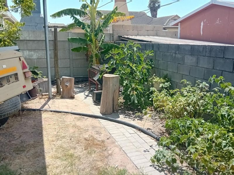 A rear garden area featuring a concrete block boundary wall and a paved walkway, currently requiring landscaping and maintenance.