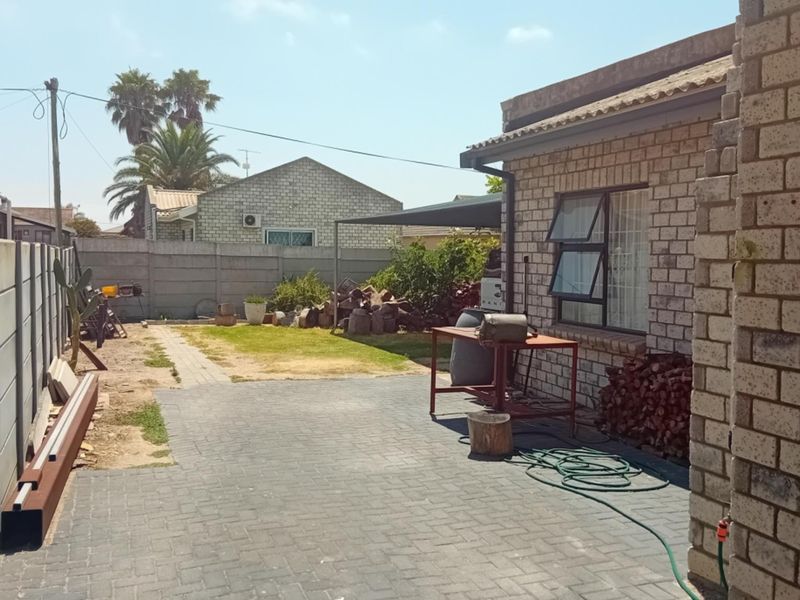 A rear exterior view featuring a paved patio area, face brick walling, and a garden space enclosed by precast concrete boundary walls.