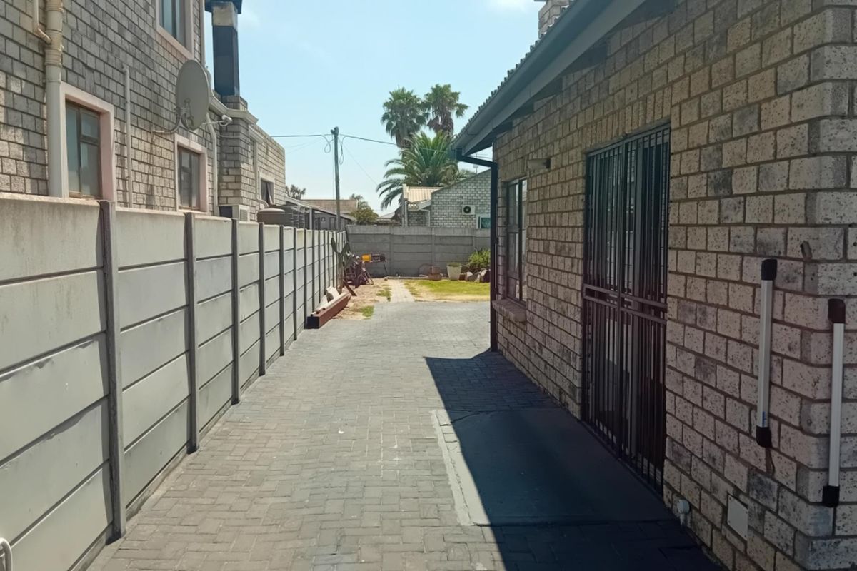 A side passage featuring paved flooring, facebrick exterior walls, and a secure metal gate, leading towards the rear garden area.