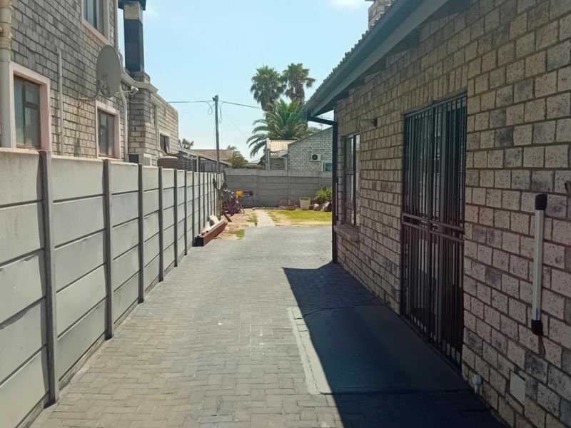 A side passage featuring paved flooring, facebrick exterior walls, and a secure metal gate, leading towards the rear garden area.