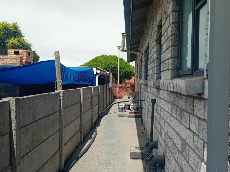 A side passage of the property featuring exposed brickwork, a precast concrete boundary wall, and external plumbing infrastructure.