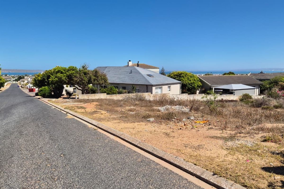 Street view of a vacant residential plot featuring a paved road, concrete curbing, and an existing boundary wall in a coastal neighborhood.