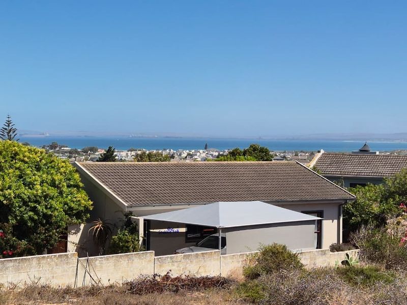 An elevated view of a residential property featuring a tiled roof, boundary wall, and carport, with a scenic coastal landscape in the background.