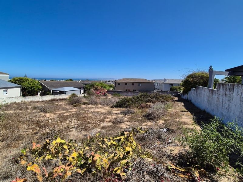 A vacant residential plot featuring a boundary wall and distant ocean views, ready for development.