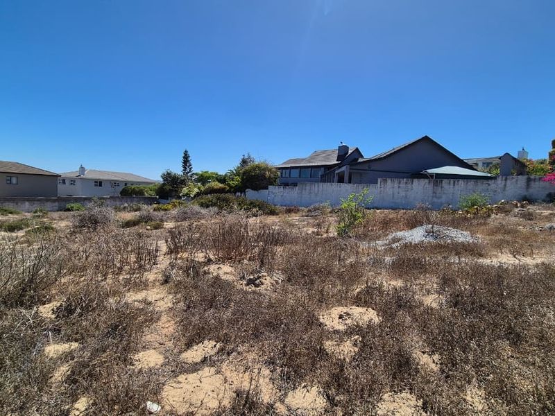 A vacant residential plot featuring sandy terrain and a perimeter boundary wall, situated in a developed neighborhood.