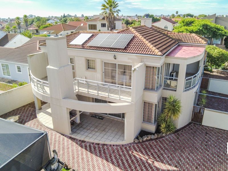 Aerial view of a two-story residential property featuring a tiled roof, solar panels, a paved driveway, and a covered patio with a built-in braai.