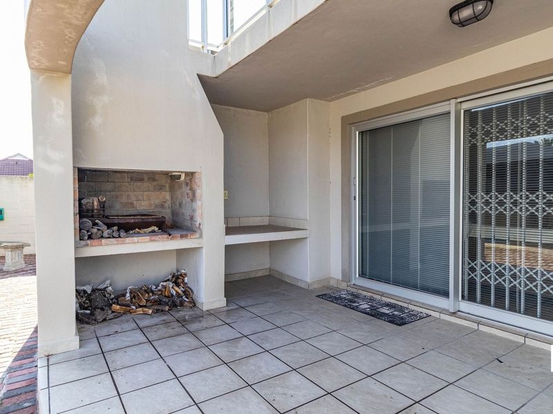 Covered patio area featuring a built-in braai, tiled flooring, and direct access to the interior through sliding glass doors.