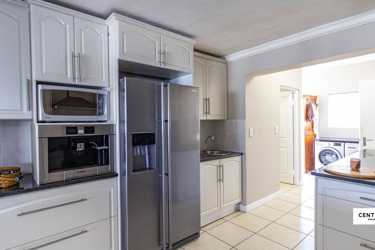 Modern kitchen featuring white cabinetry, granite countertops, built-in appliances including a microwave and coffee machine, and tiled flooring.