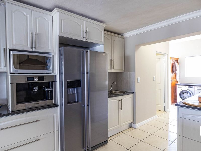 Modern kitchen featuring white cabinetry, granite countertops, built-in appliances including a microwave and coffee machine, and tiled flooring.