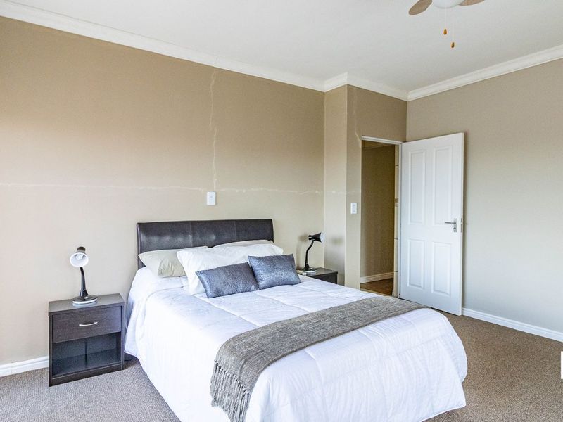 A carpeted bedroom featuring neutral walls, a ceiling fan, and a standard internal door, showing some visible wall cracking.