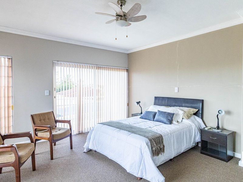 Spacious bedroom featuring neutral walls, carpet flooring, a ceiling fan, and sliding glass doors with vertical blinds leading to an outdoor area.