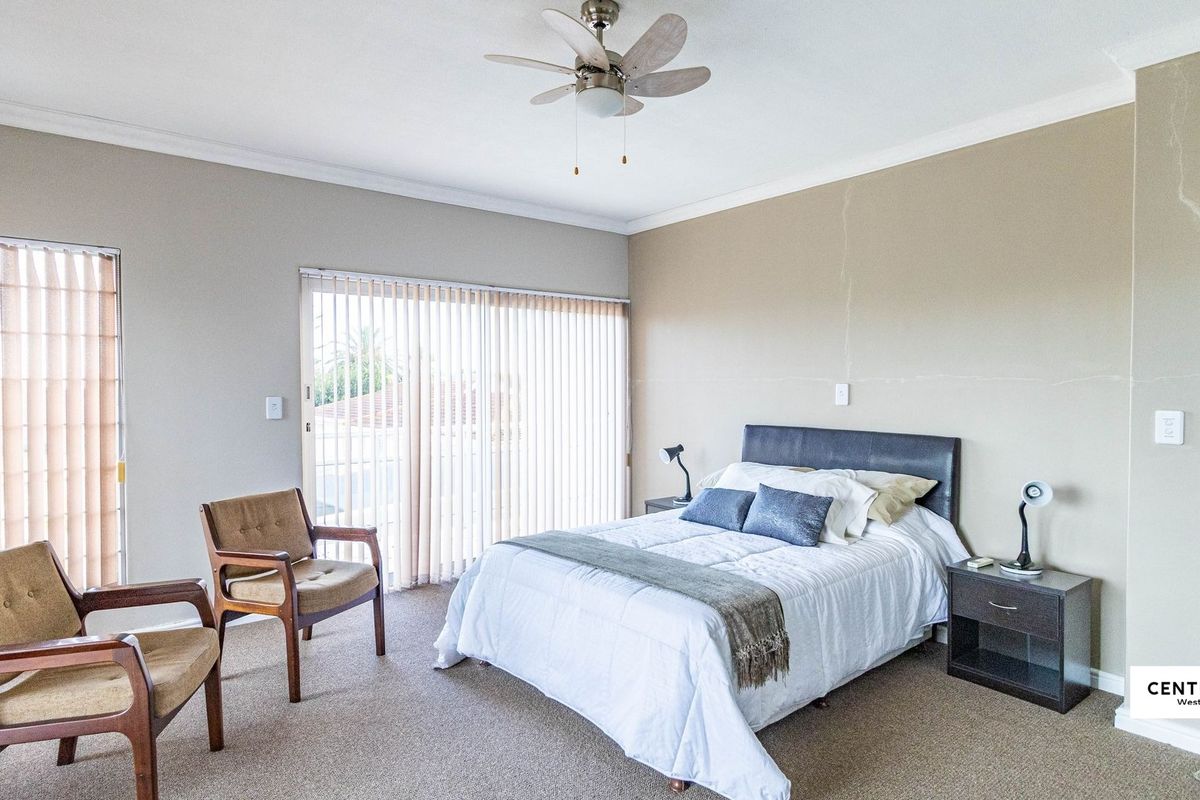 Spacious bedroom featuring neutral walls, carpet flooring, a ceiling fan, and sliding glass doors with vertical blinds leading to an outdoor area.