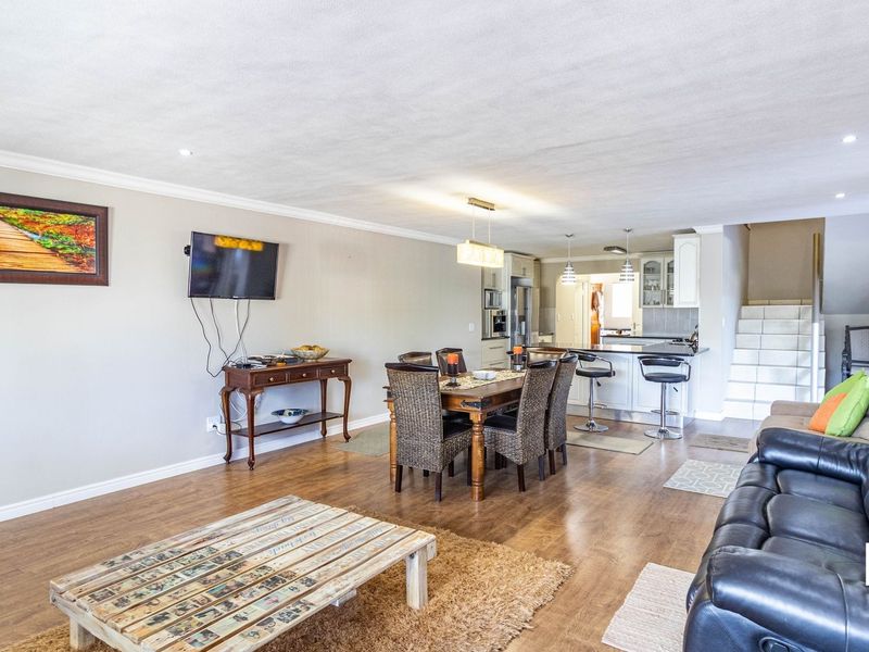 Spacious open-plan living and dining area featuring laminate flooring, a modern kitchen with an island, and a staircase leading to the upper level.