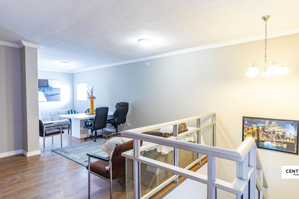 An open-plan living area featuring laminate flooring, a staircase with a modern railing, and neutral wall finishes.