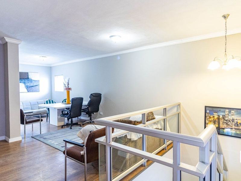 An open-plan living area featuring laminate flooring, a staircase with a modern railing, and neutral wall finishes.