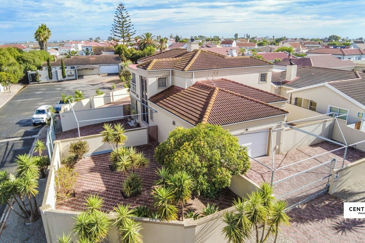 Aerial view of a residential property featuring a tiled roof, paved driveway, secure boundary walls, and an automated garage.