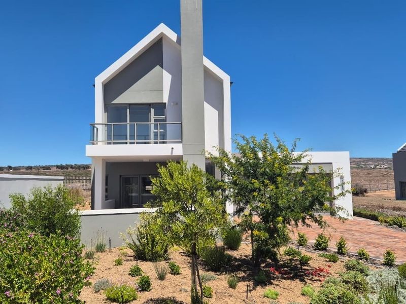 Modern two-story residential home featuring a prominent chimney, upper-level balcony with glass balustrade, and a well-maintained landscaped front garden with paved driveway.