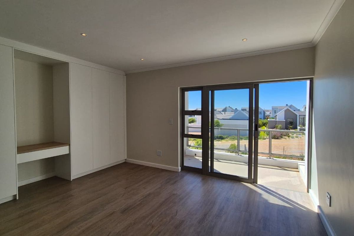 A bright, modern bedroom featuring built-in cupboards with an integrated desk, laminate flooring, and direct access to a private balcony through sliding glass doors.
