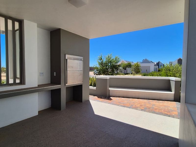 A modern covered patio featuring a built-in braai, integrated bench seating, and durable paved flooring, perfect for outdoor entertaining.