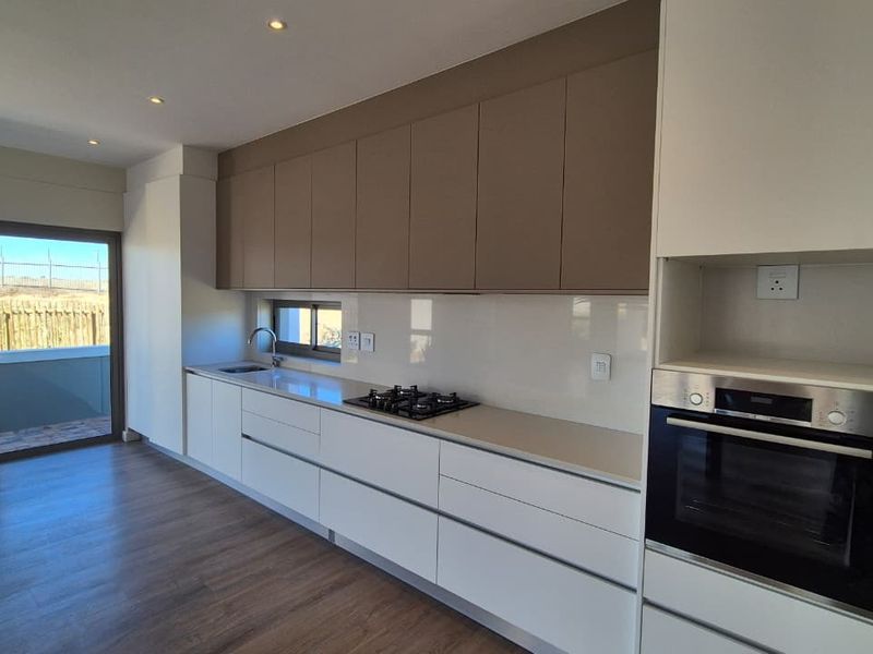 Modern kitchen featuring sleek handleless cabinetry, integrated gas hob, built-in oven, and direct access to an outdoor patio area.