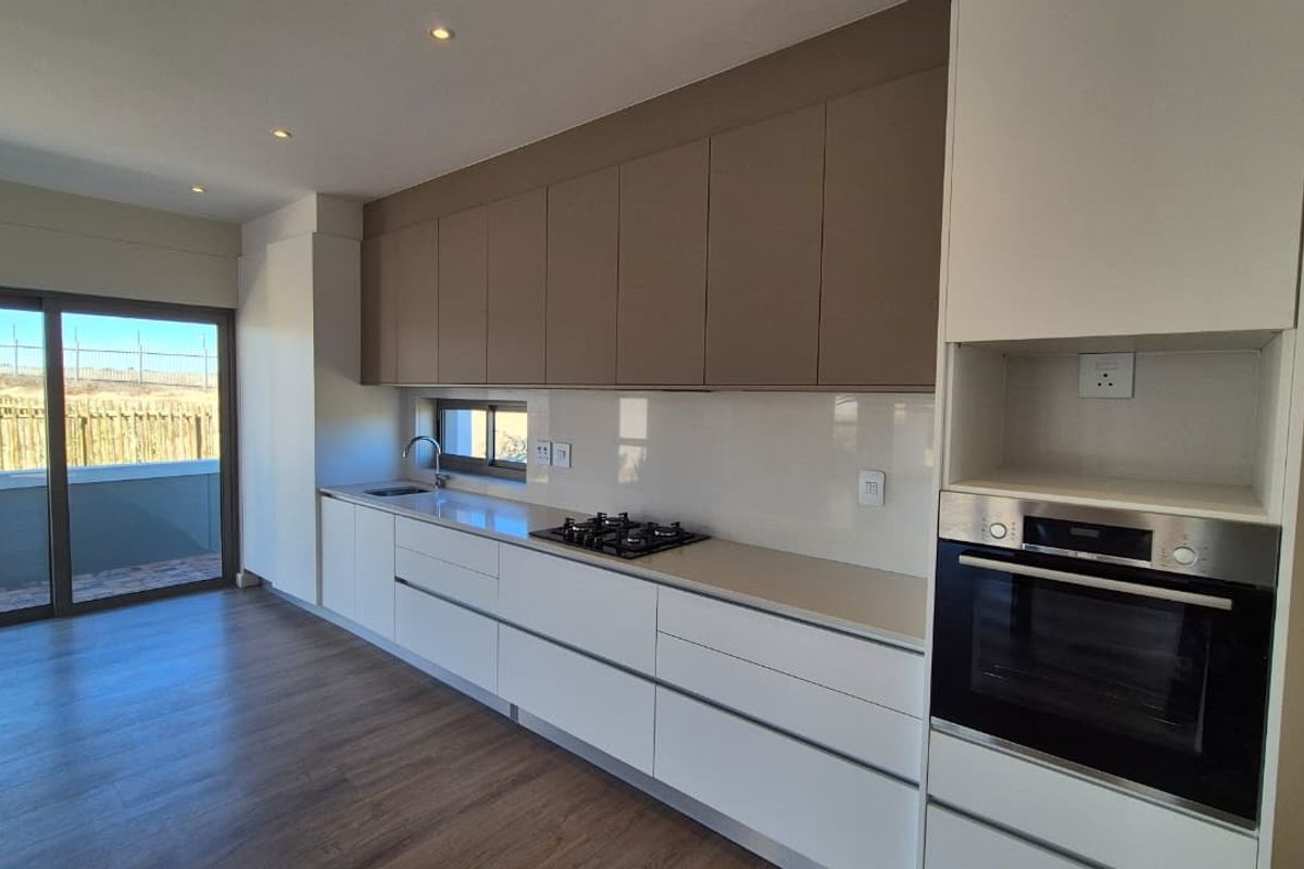 Modern kitchen featuring sleek handleless cabinetry, integrated gas hob, built-in oven, and direct access to an outdoor patio area.