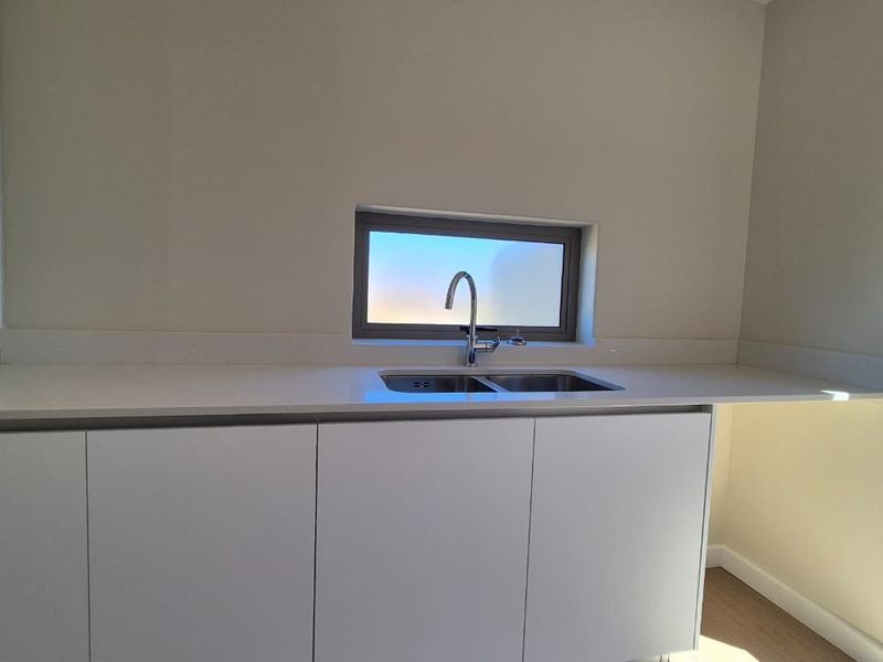 A clean, modern scullery or utility area featuring white cabinetry, a stone benchtop, and a stainless steel double sink with a chrome mixer tap.