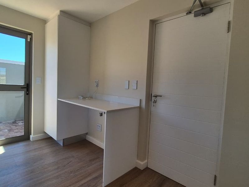 A bright, modern home office space featuring built-in desk cabinetry, laminate flooring, and direct access to an outdoor area through a glass door.