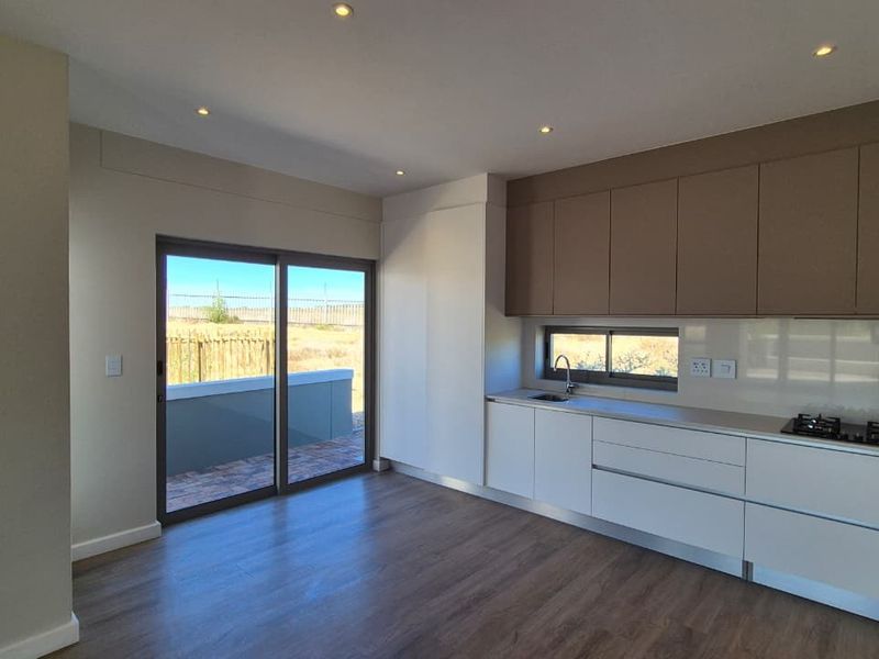 Modern open-plan kitchen featuring sleek cabinetry, a gas hob, and direct access to an outdoor patio area through sliding glass doors.