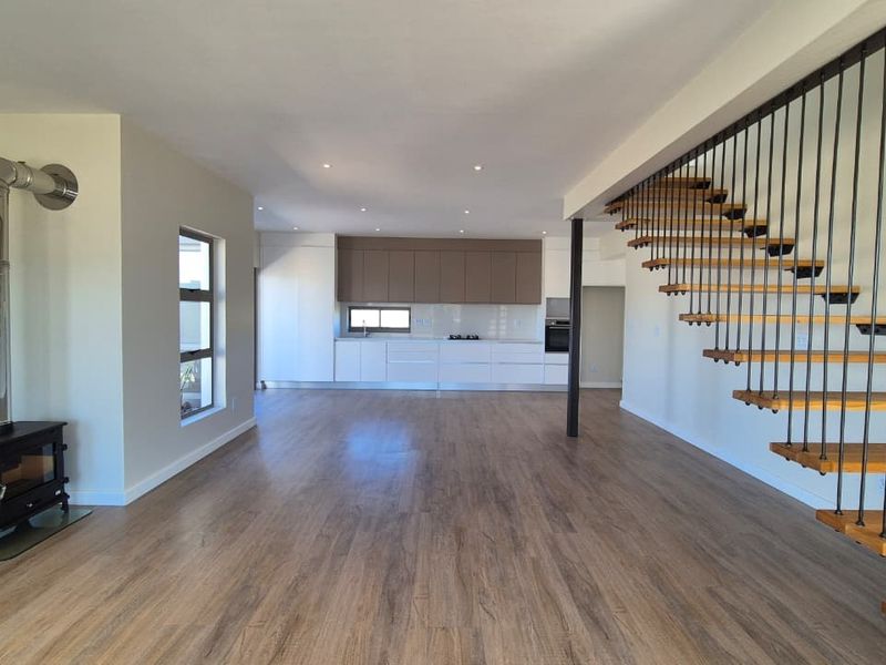 Spacious open-plan living area featuring a modern wood-burning stove, contemporary kitchen cabinetry, and a striking floating staircase with timber treads.