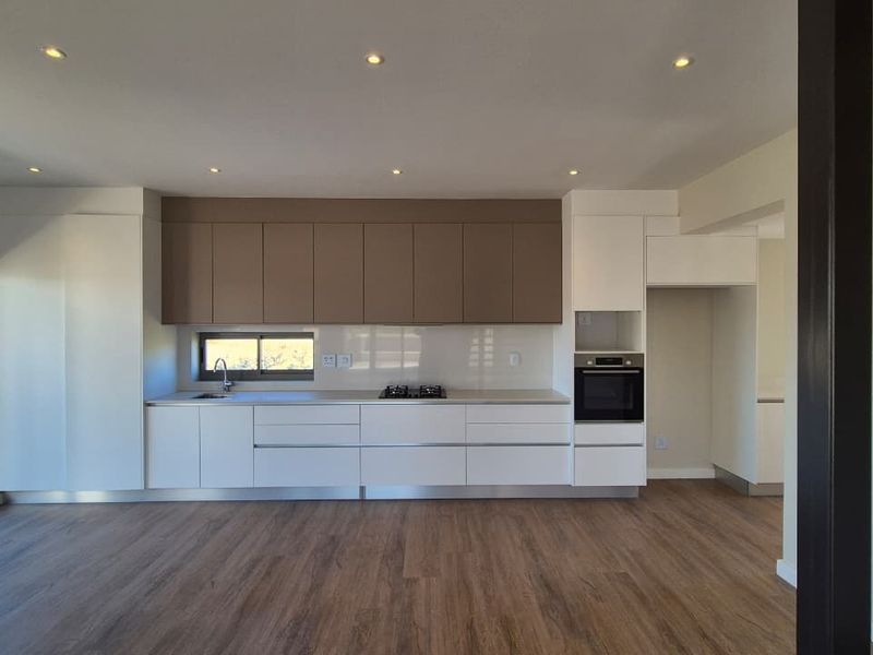 Modern open-plan kitchen featuring sleek two-tone cabinetry, integrated oven, gas hob, and wood-look laminate flooring with direct access to an outdoor area.
