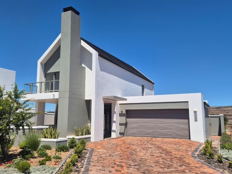 Modern double-story house featuring a brick-paved driveway, integrated double garage, prominent chimney stack, and a balcony, set within a landscaped garden.