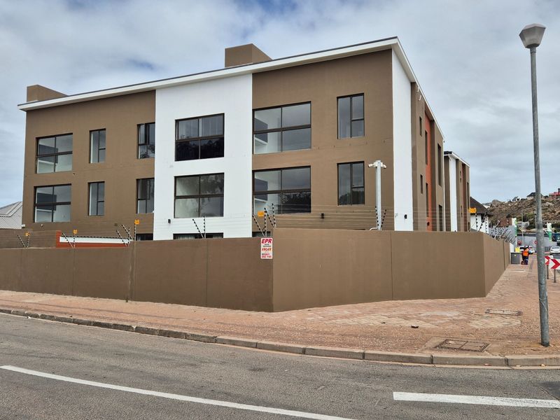 Modern multi-story apartment building exterior featuring a secure perimeter wall with electric fencing and contemporary architectural design.