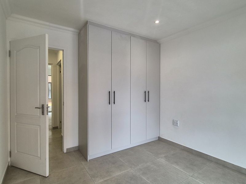 A clean, modern bedroom featuring neutral tiled flooring, built-in cupboards with contemporary handles, and recessed lighting.